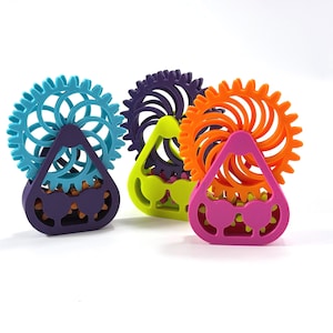 Puede incluir: Tres juguetes fidget impresos en 3D con mecanismos de engranajes circulares montados sobre bases triangulares. Los engranajes son turquesa, morado oscuro y naranja, mientras que las bases son moradas, verde lima y rosa brillante.