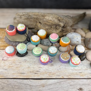 Può includere: Assortimento di ciondoli cupcake colorati con vari disegni di glassa e codette. I ciondoli sono in plastica e hanno una finitura lucida.