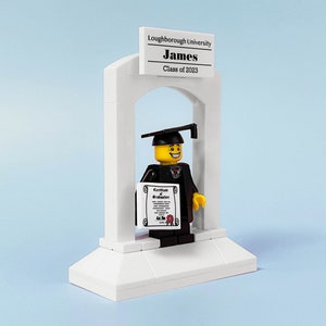 May include: A white LEGO graduation arch with a black-robed LEGO figure holding a diploma. The figure has a yellow face with a smile and a black graduation cap. The arch has a sign that reads "Loughborough University James Class of 2023".