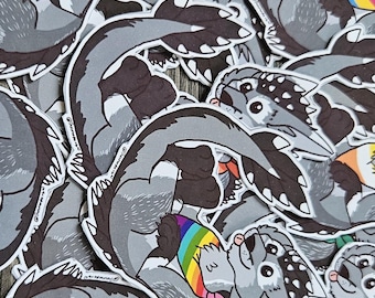 May include: A collection of die-cut stickers featuring a cartoon wolf-like creature with grey fur, dark markings, and a small tongue sticking out. Each sticker depicts the character wearing a different colored bandana representing various pride flags.