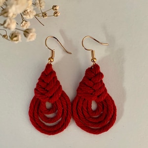 Op de afbeelding: Een paar rode, geknoopte, traanvormige oorbellen met gouden haakjes.