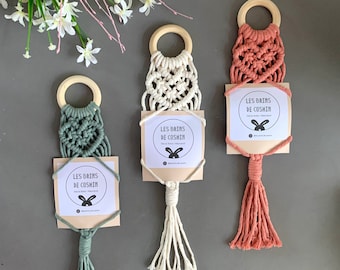 Op de afbeelding: Drie macramé wandhangers met houten ringen en kwastjes. De hangers zijn in de kleuren groen, wit en koraal. Elke hanger heeft een klein kaartje met de tekst "Les Brins de Coshkin" in het Frans.