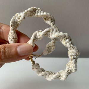 Könnte beinhalten: Ein Paar weiße Seil-Creolen mit goldenen Akzenten. Die Ohrringe bestehen aus einem dicken, geflochtenen Seil mit einem goldenen Faden, der durch das Seil gewebt ist.