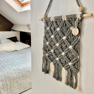 Könnte beinhalten: Graue und weiße Makramee-Wandbehänge mit einem Holzstab und einem kleinen Holzschild mit der Aufschrift "Les Envies de Créer".