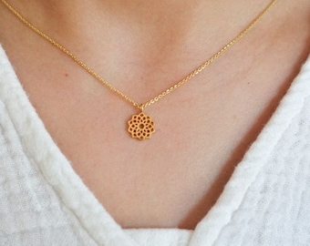 May include: A delicate gold-colored necklace featuring a small, openwork pendant with a floral design. The necklace is displayed against a white, textured fabric background, creating a simple and elegant aesthetic.