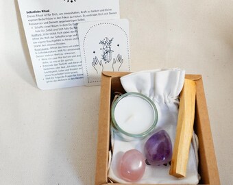 May include: A self-love ritual kit in a small brown box. The kit includes a small candle in a glass holder, a rose quartz stone, an amethyst stone, and a palo santo stick. Two cards with text and illustrations are also included.