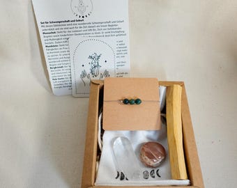 May include: A gift set in a brown box, including a bracelet with green beads, a clear crystal, a round stone, and a wooden stick. The set also contains a card with text and illustrations. The box is on a light-colored surface.