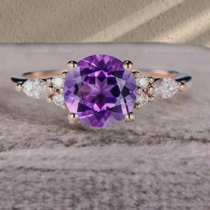 Op de afbeelding: Een verlovingsring van roségoud met een grote ronde paarse amethist als middelste steen en kleinere ronde witte diamanten op de band.