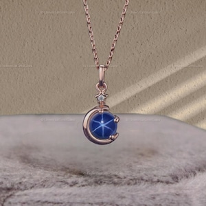 May include: A rose gold necklace with a crescent moon pendant featuring a blue star sapphire gemstone and a small diamond accent.