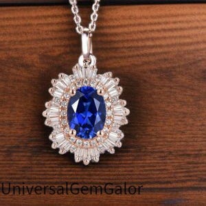 May include: A silver necklace with a pendant featuring a large, oval, deep blue gemstone surrounded by smaller, clear gemstones. The pendant is set against a wooden background. The necklace is a delicate chain.