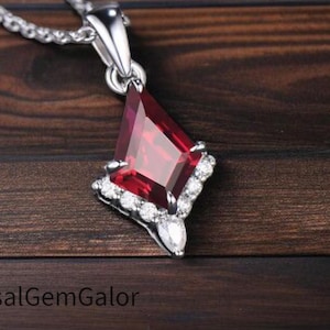 May include: A silver necklace with a pendant featuring a large, faceted, deep red gemstone in a kite shape, surrounded by smaller white gemstones. The pendant hangs from a delicate silver chain.