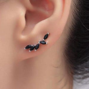 May include: A silver ear climber earring featuring a series of black marquise-cut stones. The earring curves along the ear, creating a delicate, nature-inspired design. The black stones contrast with the silver setting, offering a modern and elegant look.