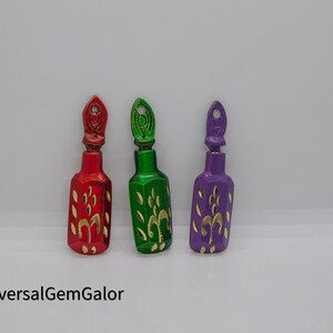 May include: Three small decorative bottles with gold accents and floral designs. The bottles are red, green, and purple.