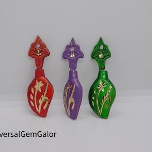 Könnte beinhalten: Drei dekorative Flaschenverschlüsse mit Blumendesigns. Die Verschlüsse sind aus Metall und in Rot, Lila und Grün lackiert. Jeder Verschluss hat ein goldenes Blumendesign.