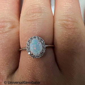 May include: A silver ring with a white oval opal gemstone surrounded by a halo of smaller white gemstones.