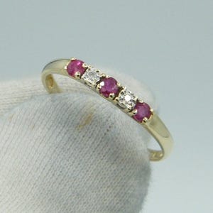 Peut inclure: Une bague en or ornée de cinq pierres précieuses. La bague alterne des rubis rouges et des diamants étincelants. Les pierres sont disposées en rangée. La bague est présentée sur fond blanc.