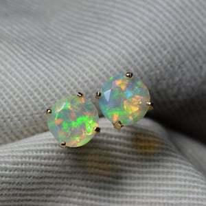 May include: A pair of opal stud earrings with a gold setting. The opals are a light green colour with flashes of rainbow.