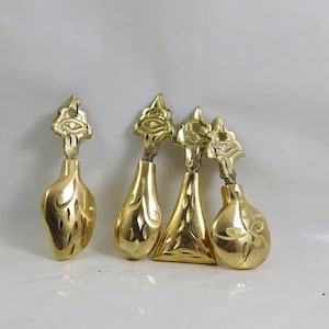 Peut inclure: Quatre tirettes de tiroir décoratives en métal couleur or avec des motifs complexes. Chaque tirette présente un œil stylisé en haut et un motif unique en bas.