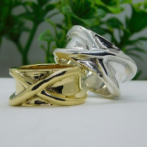 Könnte beinhalten: Zwei Ringe, einer aus Gold und einer aus Silber, mit einem Kreuzmuster. Die Ringe sind übereinander gestapelt.