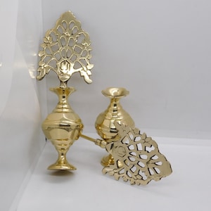 May include: Two gold metal decorative perfume bottles with intricate filigree designs on the tops. The bottles have a round body and a flared base.