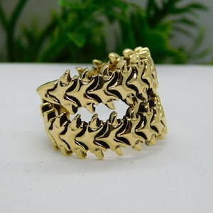 May include: A gold-toned ring with a unique design featuring a series of interlocking, pointed shapes that resemble teeth or scales.