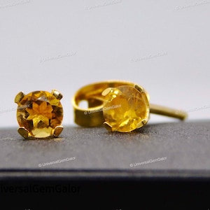 以下が含まれることがあります： 丸いファセットカットのオレンジ色の宝石が付いた、ゴールドのスタッドピアスのペアです。