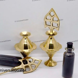 Pode incluir: Dois recipientes decorativos de metal dourado com uma parte superior pontiaguda e uma pequena garrafa cheia de pó preto. Os recipientes têm uma base redonda e um design decorativo na parte superior.