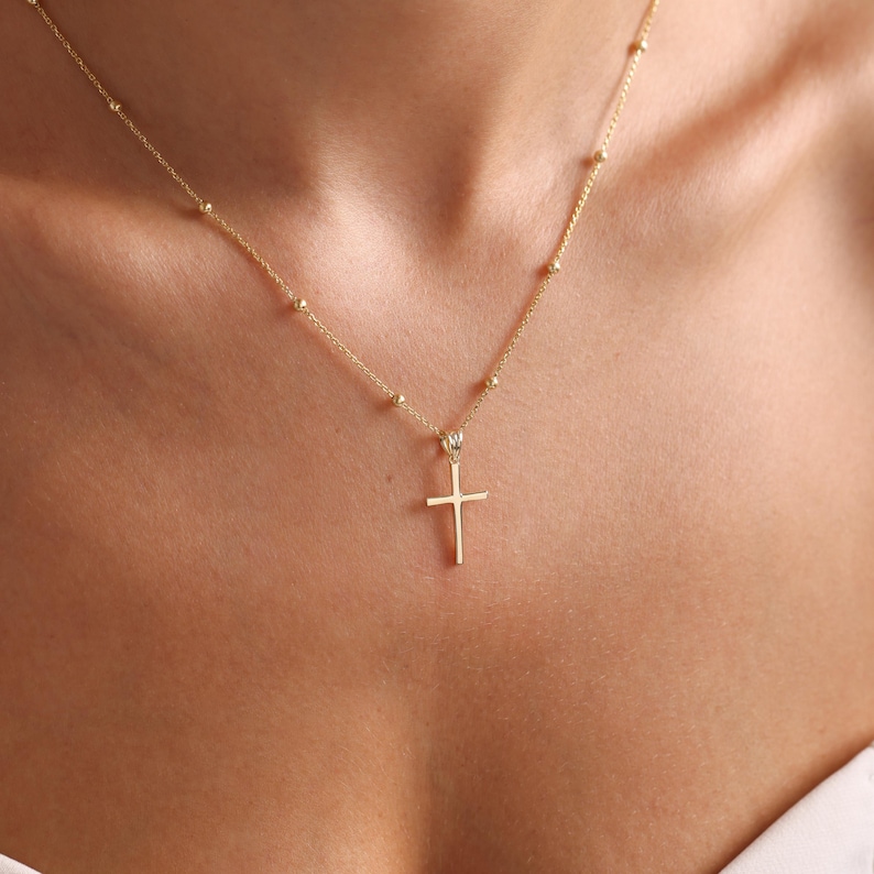 May include: A gold chain necklace with a small, simple cross pendant.