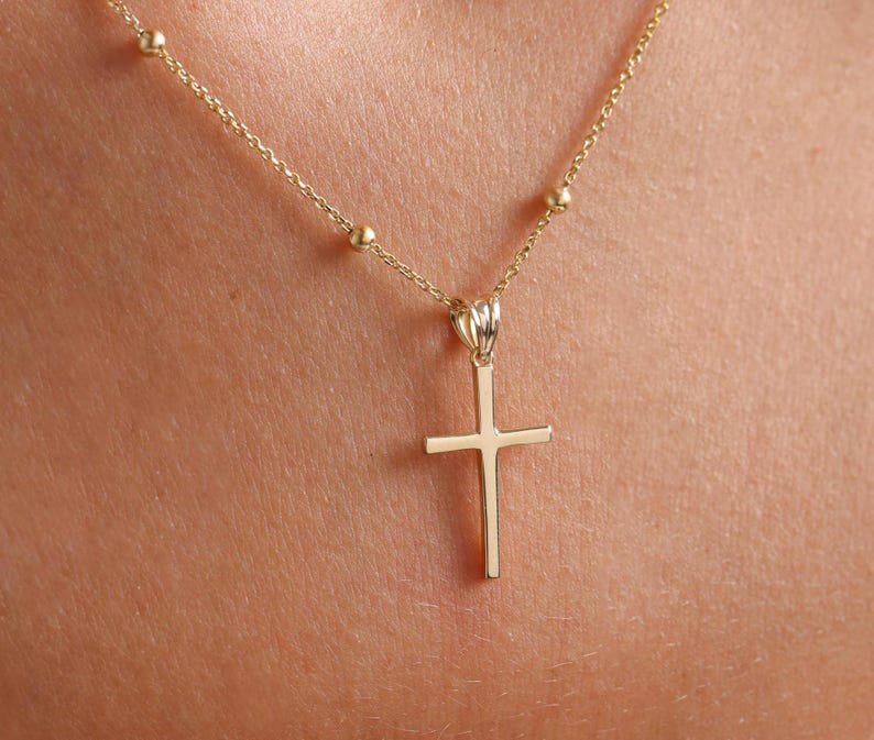 May include: A gold chain necklace with a small gold cross pendant.