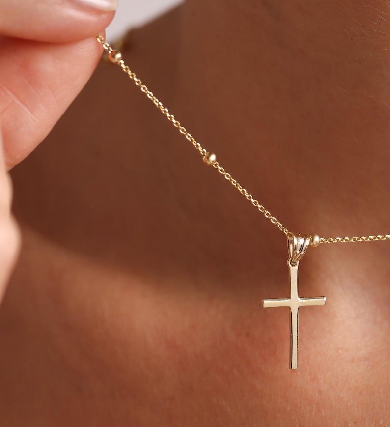May include: A gold chain necklace with a small gold cross pendant. The chain has small round beads.
