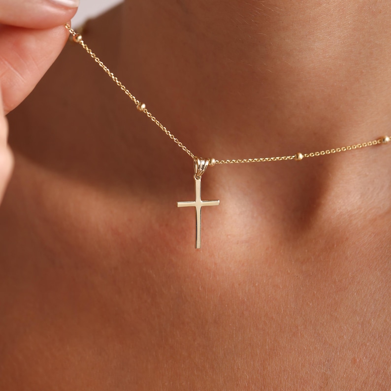 May include: A gold chain necklace with a small, simple cross pendant. The chain features small, round beads.