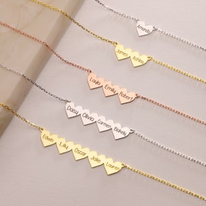 May include: A collection of personalized heart necklaces in gold, silver, and rose gold. Each necklace features heart-shaped pendants with engraved names, connected by delicate chains. The names include Amanda, James, Ashley, Layla, Emily, Robert, Daisy, Olivia, Carmen, Blakely, Edwin, Lily, Oscar, Jolie, and Lauren.