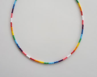 May include: A rainbow beaded choker necklace with a gold clasp. The necklace is made of small, colorful beads in a rainbow pattern.