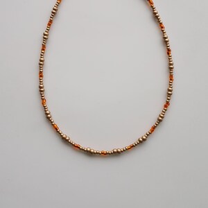 Puede incluir: Un collar de oro con pequeñas cuentas redondas y algunas cuentas naranjas.