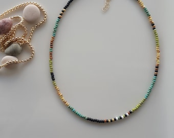 May include: A delicate beaded necklace with a gold clasp. The necklace features a multi-colored pattern of black, white, green, and brown beads.