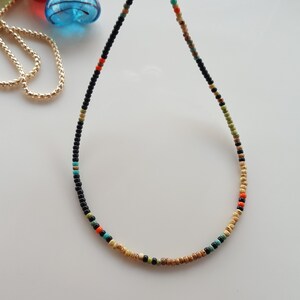 May include: A delicate beaded necklace with black, brown, orange, and turquoise beads.