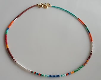May include: A colorful beaded necklace with a gold clasp. The necklace is made of small, round beads in shades of red, orange, yellow, green, blue, and white.