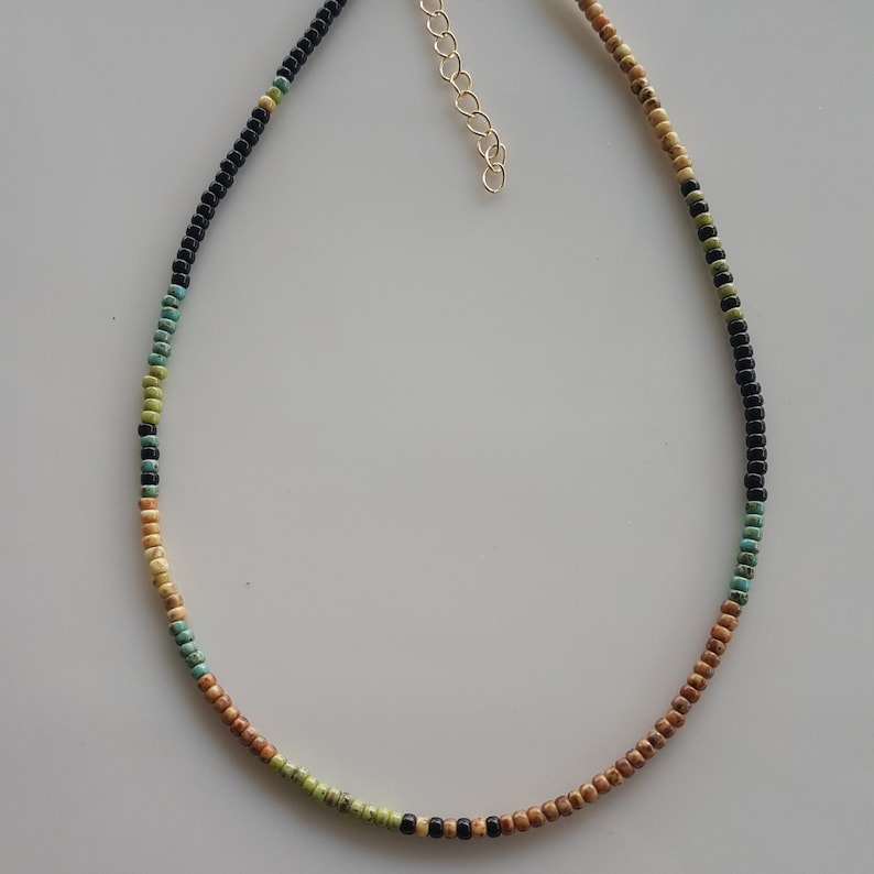 May include: A multi-coloured beaded necklace with black, brown, green and turquoise beads. The necklace is made of small, round beads and has a gold chain clasp.