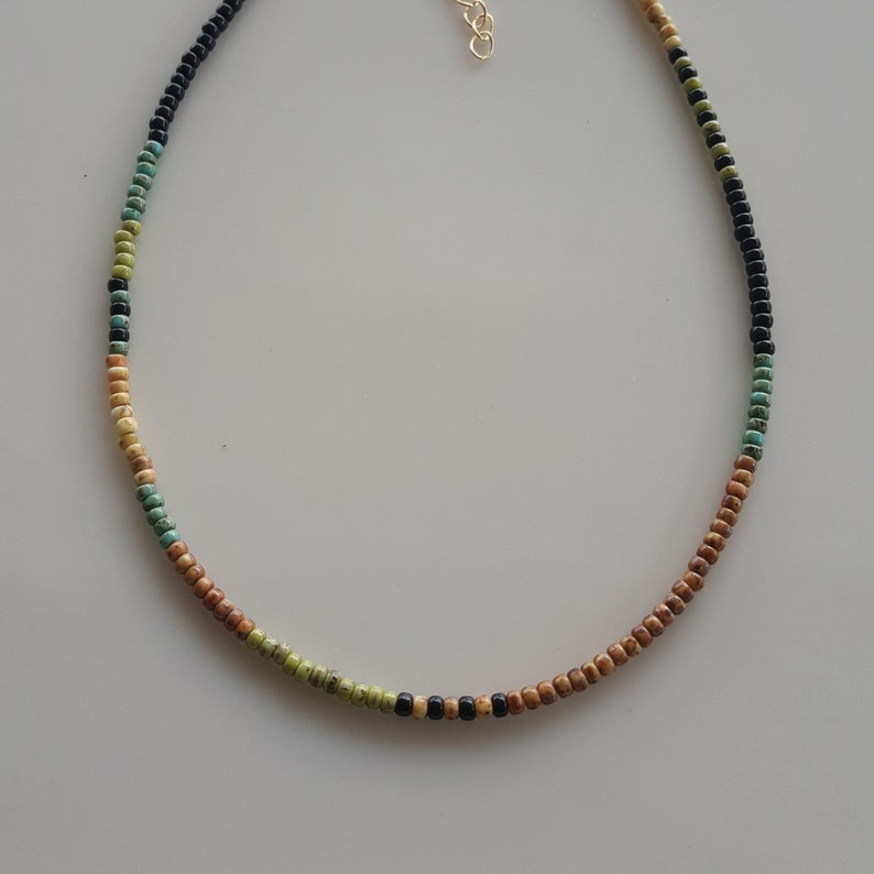 May include: A multi-coloured beaded necklace with brown, green and black beads. The necklace is made of small, round beads and has a simple design.