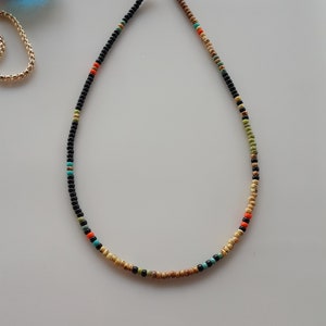 May include: A beaded necklace with black, beige, orange, green, and turquoise beads.