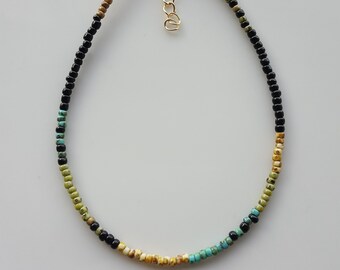 May include: A delicate beaded necklace with black, turquoise, yellow, and green beads. The necklace has a gold clasp.
