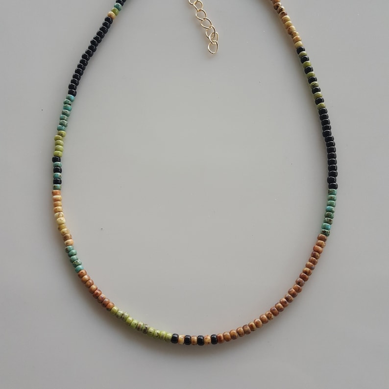 May include: A multi-coloured beaded necklace with brown, green and black beads. The necklace is made of small, round beads and has a gold clasp.