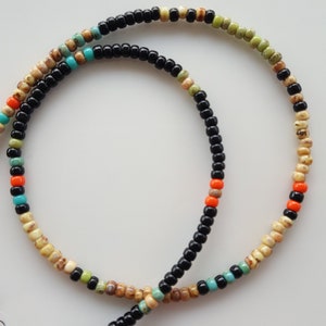 May include: A multi-colored beaded necklace with black, beige, orange, and turquoise beads.