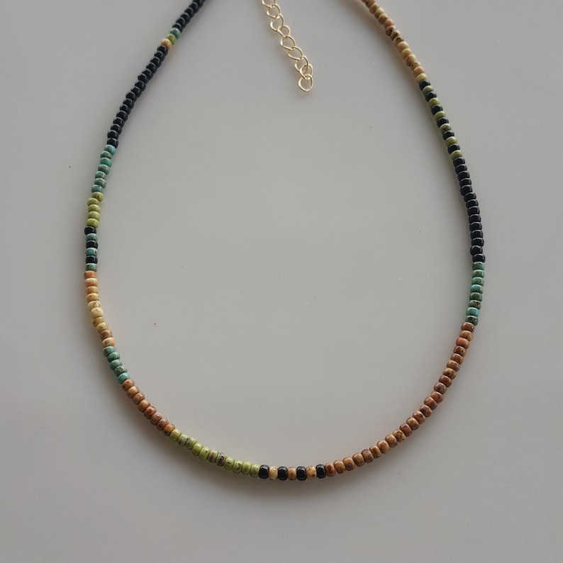 May include: A multi-coloured beaded necklace with brown, green, turquoise, and black beads. The necklace has a gold clasp.
