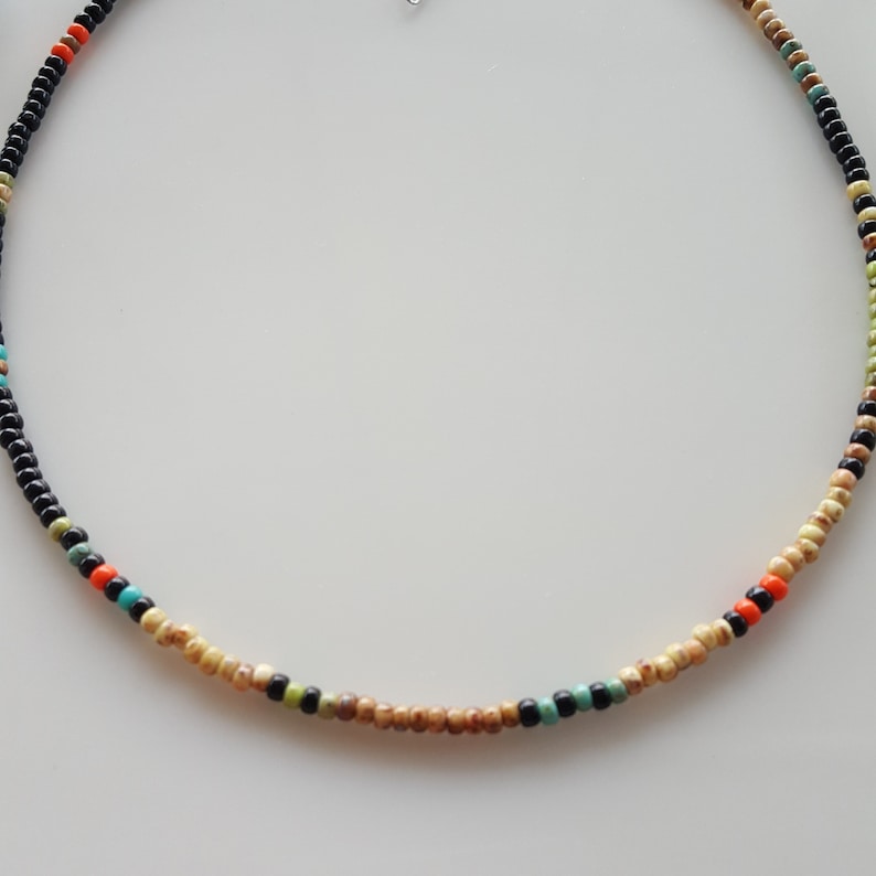 May include: A beaded necklace with black, beige, orange, turquoise, and green beads.