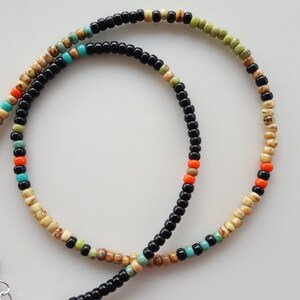 May include: A layered necklace with black, beige, orange, and turquoise beads. The necklace is made of small, round beads and has a simple, minimalist design.