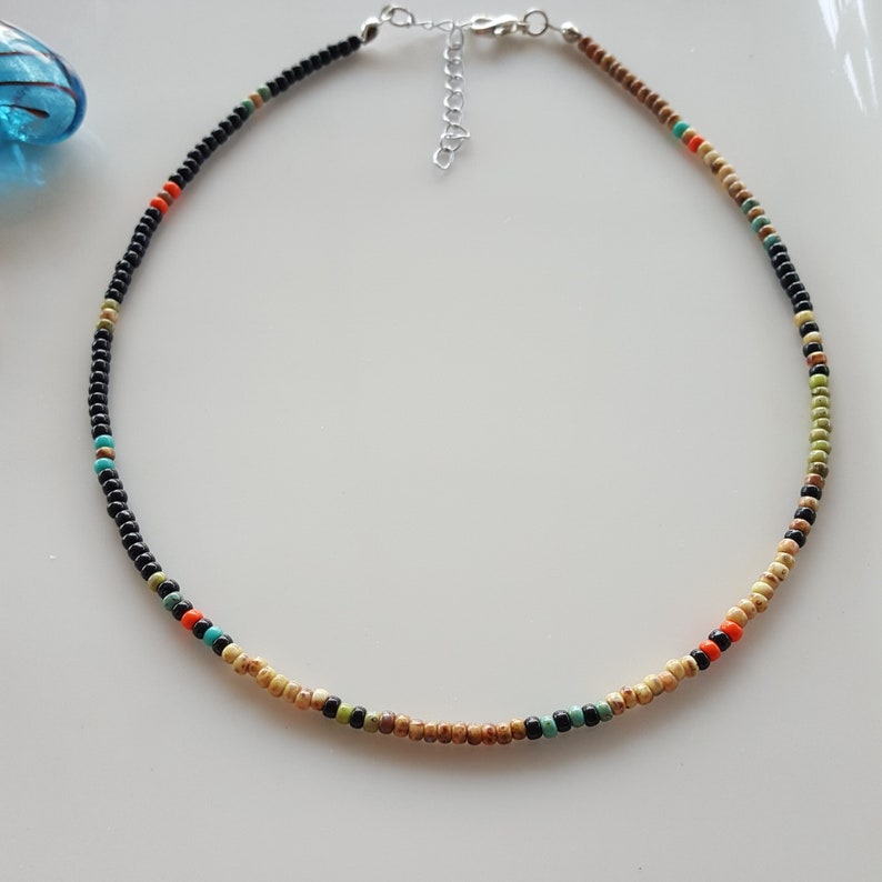 May include: A delicate choker necklace with black, beige, green, orange, and turquoise beads. The necklace has a silver clasp.