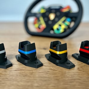 May include: Four black plastic stands with different colored stripes. The stands are designed to hold a steering wheel. The stripes are silver, blue, gold, and red.