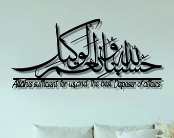 May include: A white couch with pillows in a living room setting. The wall behind the couch has a black calligraphy design with the text "Allah is sufficient for us and the best Disposer of affairs". The design is framed by a thin black line. The floor is wood with a brown rug and a small round woven ottoman. There is a gold metal side table with two tiers.