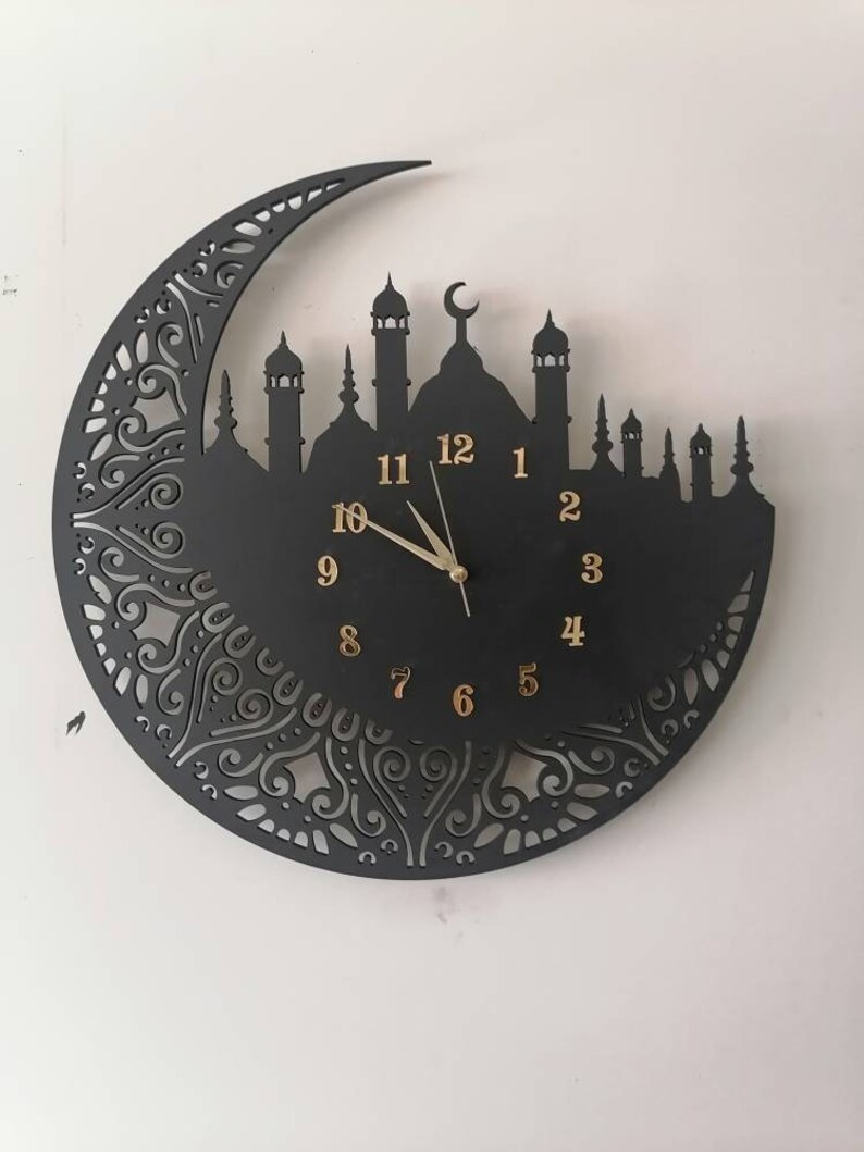 May include: Black wall clock with a crescent moon design and a mosque silhouette. The clock face has gold Arabic numerals and a gold hour and minute hand.